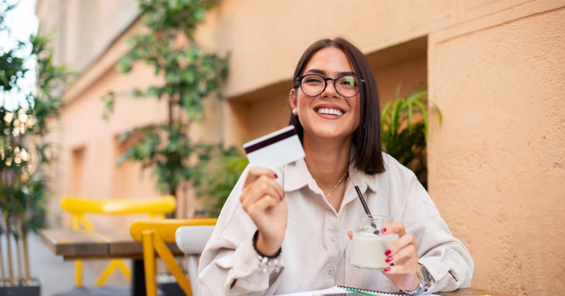 Una mujer sonriendo mostrando una tarjeta de crédito